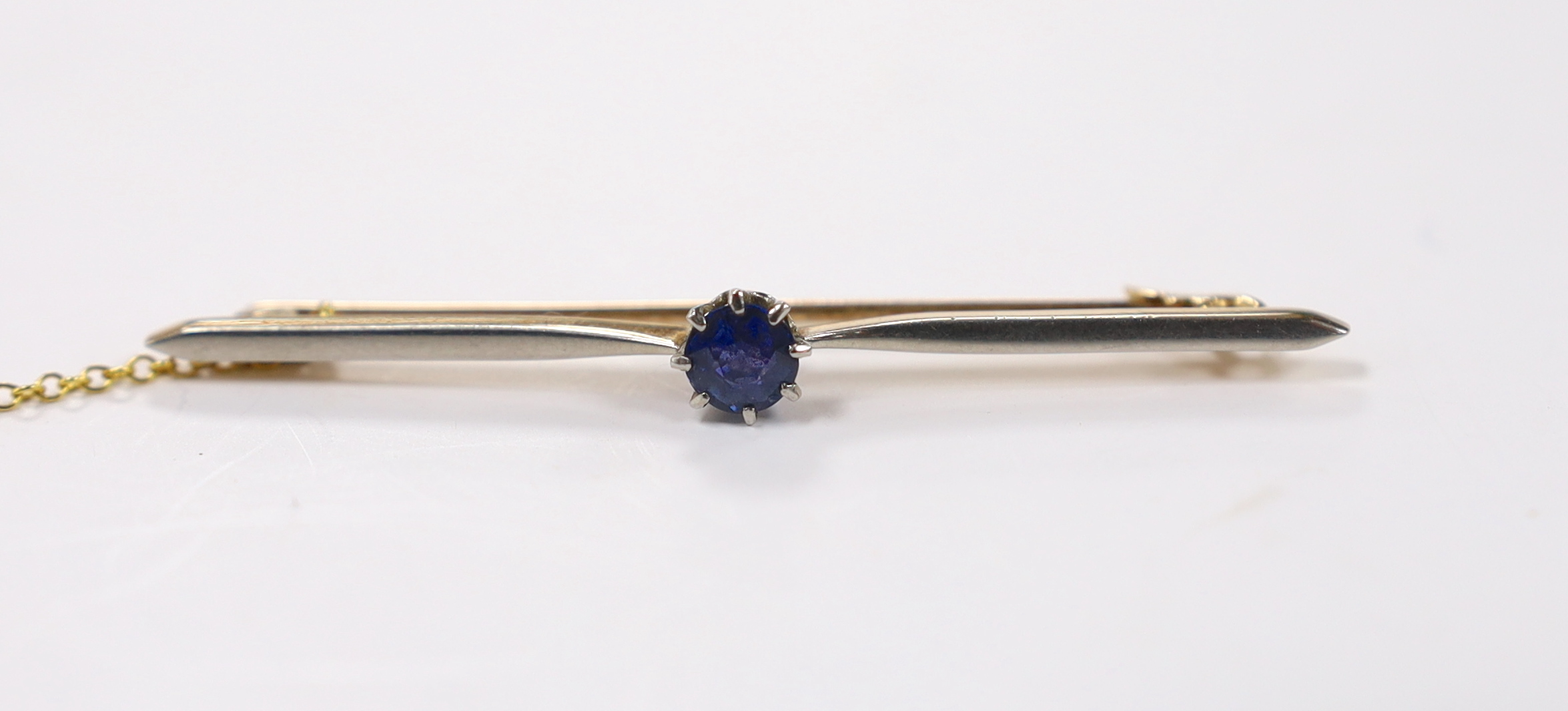 An early 20th century yellow metal and single stone sapphire set bar brooch, 57mm, gross weight 4.2 grams, with safety chain.